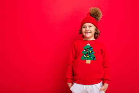 cheerful funny boy on a red background in a warm hat and sweater with a Christmas tree.の写真素材