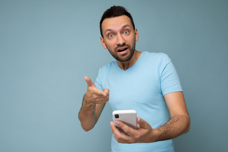 Photo of amazed asking handsome young man with beard wearing everyday blue t-shirt isolated over...