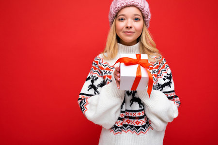 Beautiful happy young blonde woman isolated over colourful background wall wearing stylish casual clothes holding gift box and looking at camera. Copy space, mockupの写真素材
