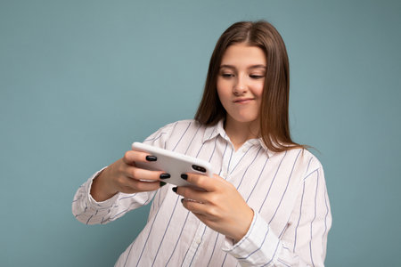 Concentrated happy attractive young blonde woman wearing casual white shirt isolated over blue...