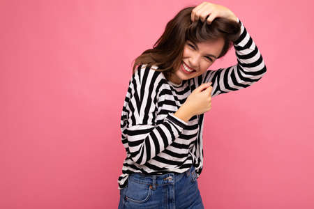 Young beautiful brunet woman. Trendy lady in casual striped longsleeve. Positive female shows facial...