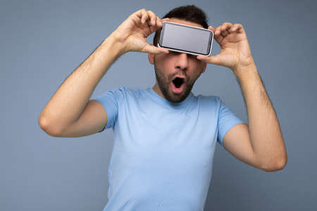 Positive amazed handsome young unshaven brunet man with beard wearing everyday blue t-shirt isolated...