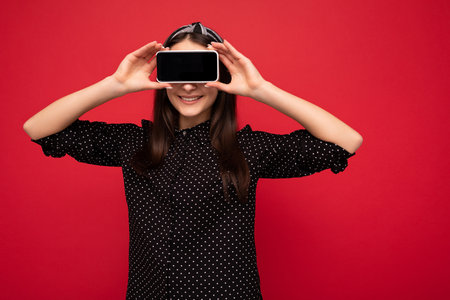Pretty smiling joyful brunette girl standing isolated over red wall wearing casual stylish black...