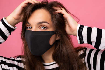Shot portrait of young brunette attractive woman wearing mediacal face mask isolated over background...