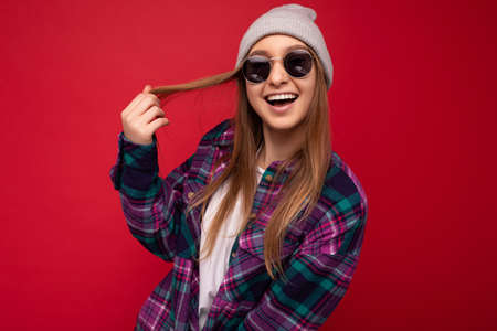 Photo shot of beautiful positive happy young dark blonde woman isolated over red background wearing...