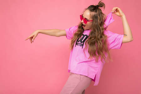 Photo shot of beautiful joyful young dark blonde woman wearing casual clothes and stylish sunglasses isolated over colorful background looking to the side and having fun.の写真素材