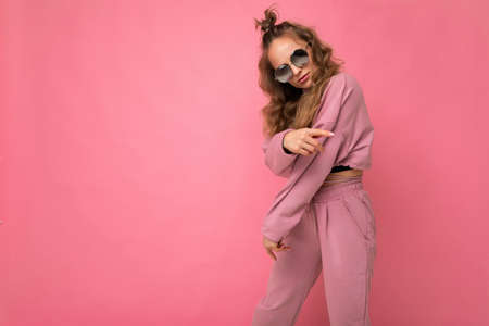 Attractive joyful young blonde woman wearing everyday stylish clothes and modern sunglasses isolated on colorful background wall looking at camera. copy spaceの写真素材