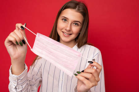 Happy young woman holds and wears a white medical mask to protect yourself from corona virus, cares...