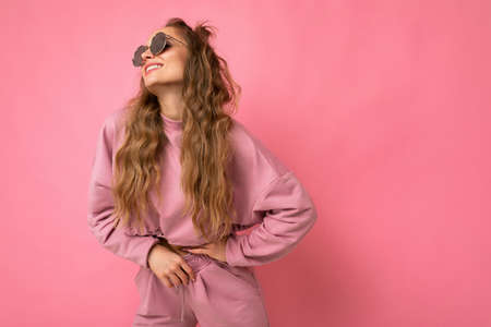 Attractive positive young blonde woman wearing everyday stylish clothes and modern sunglasses isolated on colorful background wall looking to the side. empty spaceの写真素材