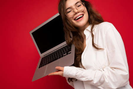 Smiling happy beautiful brunette curly young woman holding computer laptop wearing glasses white...