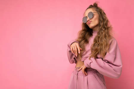 Attractive funny amusing young blonde woman wearing everyday stylish clothes and modern sunglasses isolated on colorful background wall looking to the sideの写真素材