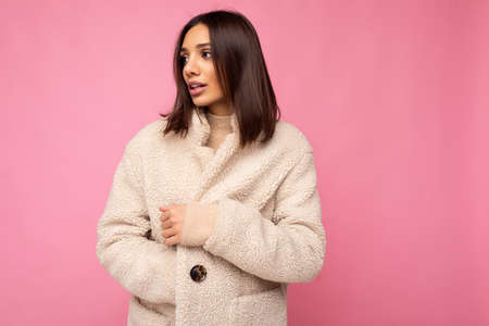 Portrait of attractive self-confident positive good-looking stylish young brunette woman wearing winter beaige warm coat isolated on pink background with free space. Fashion conceptの写真素材