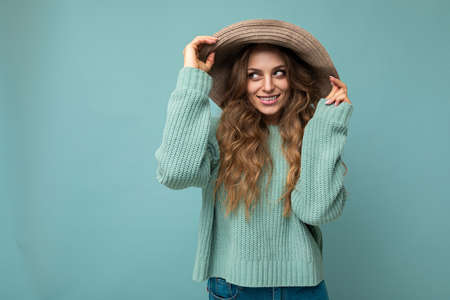 Portrait of young beautiful smiling hipster woman in trendy outfit and hat. Sexy carefree female person posing isolated near blue wall in studio with free space. Positive model with natural makeupの写真素材
