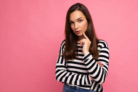 Shot of thoughtful beautiful young woman deep thinking creative female person holding arm on chin wearing stylish outfit isolated on colorful background with copy spaceの写真素材