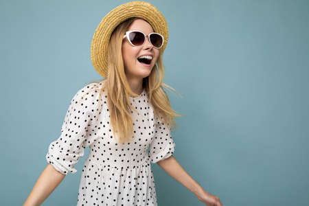 Photo shot of beautiful positive young blonde woman wearing summer casual clothes and stylish sunglasses isolated over colorful background looking to the sideの写真素材