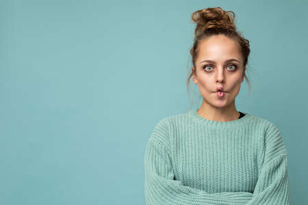 Shot of young funny joyful happy pretty blonde woman wearing blue jersey isolated on blue background with empty space and having funの写真素材