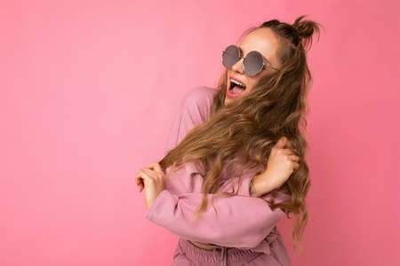 Shot of beautiful happy emotionsl young dark blonde curly woman isolated over pink background wall...