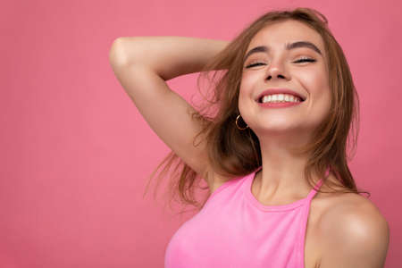 Closeup of smiling young beautiful dark blonde woman with sincere emotions isolated on background wall with copy space wearing stylish pink top. Positive conceptの写真素材