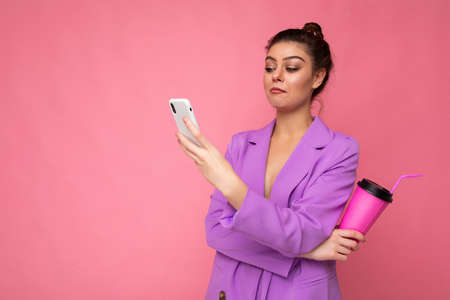 Young amazed shocked woman isolated over pink background with copy space holding coffee to take away and a mobile phoneの写真素材