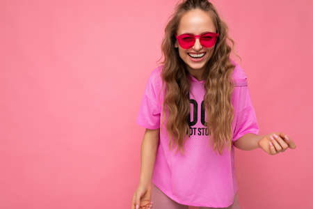 Photo shot of beautiful happy smiling young dark blonde woman wearing casual clothes and stylish sunglasses isolated over colorful background looking at cameraの写真素材