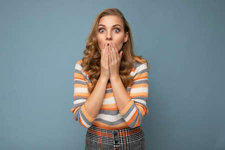 Portrait of young shocked blonde beautiful curly woman with sincere emotions wearing striped sweater...