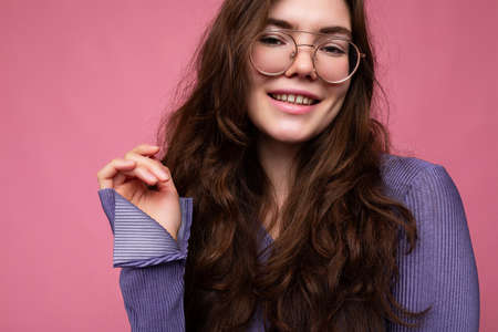 Photo shot of beautiful positive young brunette woman wearing casual clothes and stylish optical glasses isolated over colorful background wall looking at cameraの写真素材