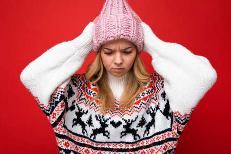 Photo of beautiful angry upset young blonde woman isolated over red background wall wearing winter sweater and pink hat looking downの写真素材