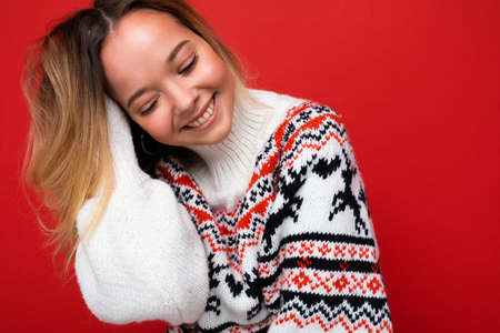 Young beautiful woman. Trendy woman in casual winter sweater. Positive female shows facial emotions. Funny model isolated on red backgroundの写真素材