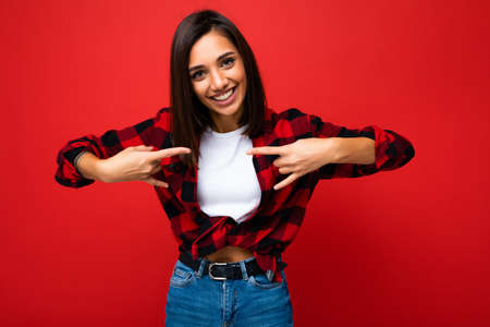 Photo of adult happy positive cool attractive brunette lady with sincere emotions wearing white t-shirt and hipster red check shirt isolated on red background with empty space and having funの写真素材
