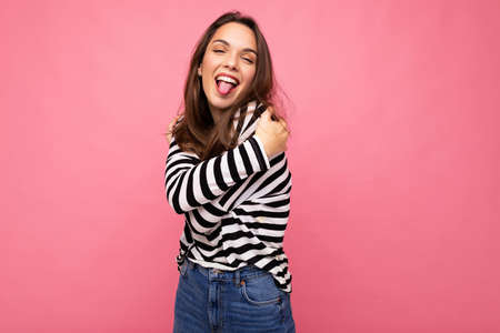 Photo shot of cute attractive pretty young funny amusing brunette woman wearing casual striped longsleeve isolated over colorful background with copy space and showing tongueの写真素材