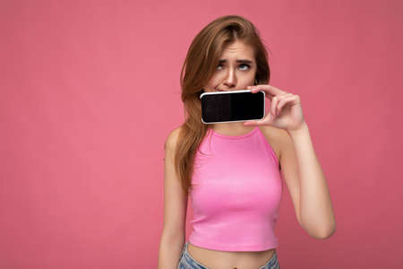 beautiful young blonde woman wearing pink top poising isolated on pink background with empty space...