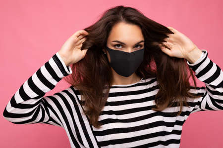 Young beautiful woman in reusable virus protective mask on face against coronavirus isolated on the pink background wallの写真素材
