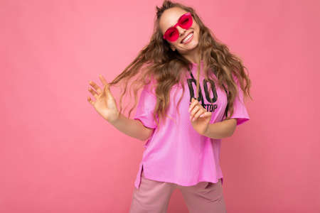 Pretty positive smiling young blonde curly woman isolated over pink background wall wearing casual...
