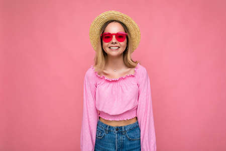 Photo shot of beautiful positive young blonde woman wearing summer casual clothes and stylish sunglasses isolated over colorful background looking at cameraの写真素材