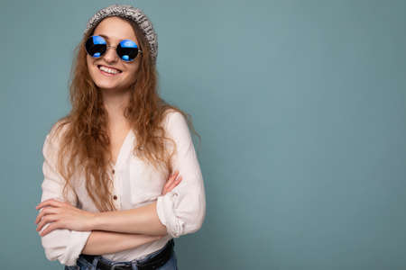 Photo shot of beautiful positive young blonde woman wearing casual clothes and stylish optical glasses isolated over colorful background wall looking at cameraの写真素材
