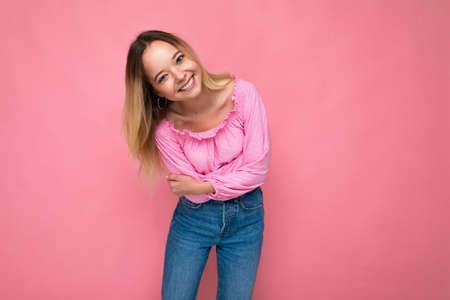 Photo shot of young beautiful cute happy blonde woman wearing stylish pink crop top isolated over pink background with copy spaceの写真素材
