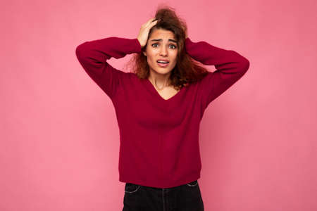 Portrait of young emotional amazed shocked beautiful brunette curly woman with sincere emotions wearing trendy pink pullover isolated on pink background with copy spaceの写真素材