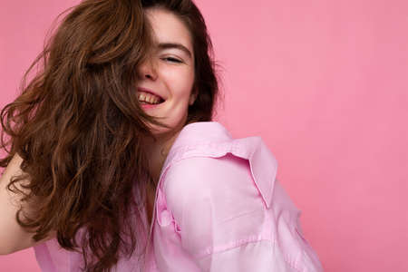 Portrait of beautiful happy smiling positive young curly brunette woman wearing pink shirt and grey hat isolated on pink background with copy spaceの写真素材