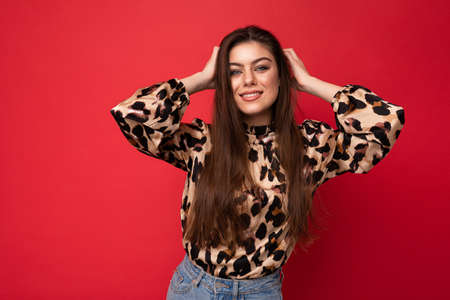 Photo of young happy smiling beautiful fashionable sexy brunette woman wearing stylish leopard blouse isolated on red background with empty spaceの写真素材