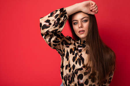 Fashion photo of young beautiful fashionable sexy brunette woman wearing stylish leopard blouse isolated on red background with empty spaceの写真素材
