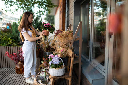 happy caucasian young woman chooses potted flowers to buy at outdoor garden stallの写真素材