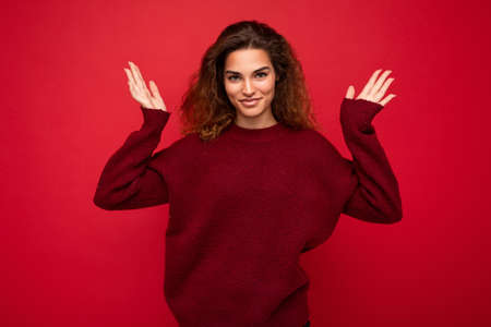 Young beautiful curly brunette woman with sincere emotions poising isolated on background wall with copy space wearing casual dark red sweater. Happy conceptの写真素材