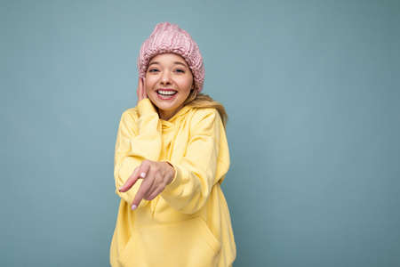 Attractive smiling happy young blond woman standing isolated over colorful background wall wearing...