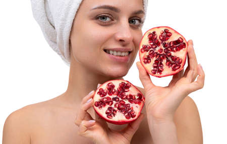 close-up of a beautiful middle-aged woman with a cut pomegranate in her hands on a white background, cosmetics and skin care conceptの写真素材