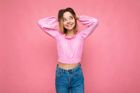 Photo shot of young beautiful cute happy blonde woman wearing stylish pink crop top isolated over pink background with copy spaceの写真素材