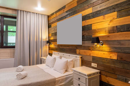 interior of a bedroom with a double bed, a picture above the headboard a wall of wooden panels in natural warm shadesの写真素材