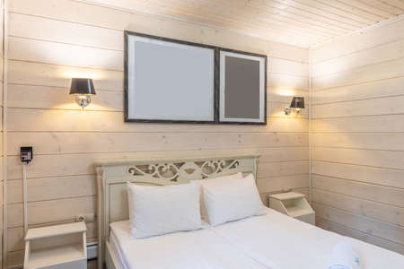 interior of a bedroom with a double bed, paintings on the headboard, decoration of the room with natural wood of light colorの写真素材