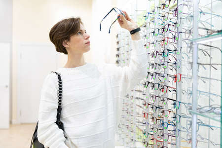 young woman near stand of eyeglasses in ophthalmologist salon
