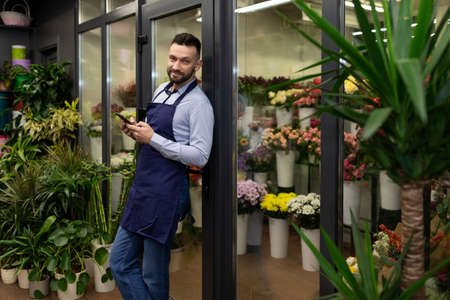 a satisfied professional florist in blue aprons next to the fridge of fresh flowers of luxury bouquetsの写真素材