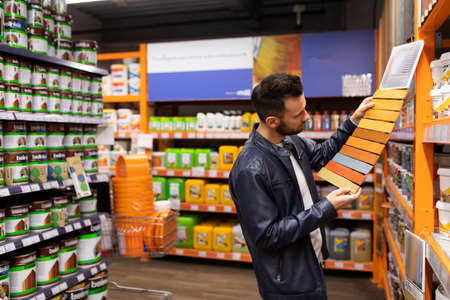 a buyer in a hardware store selects paint and varnish for renovation, looks at the color palette in...